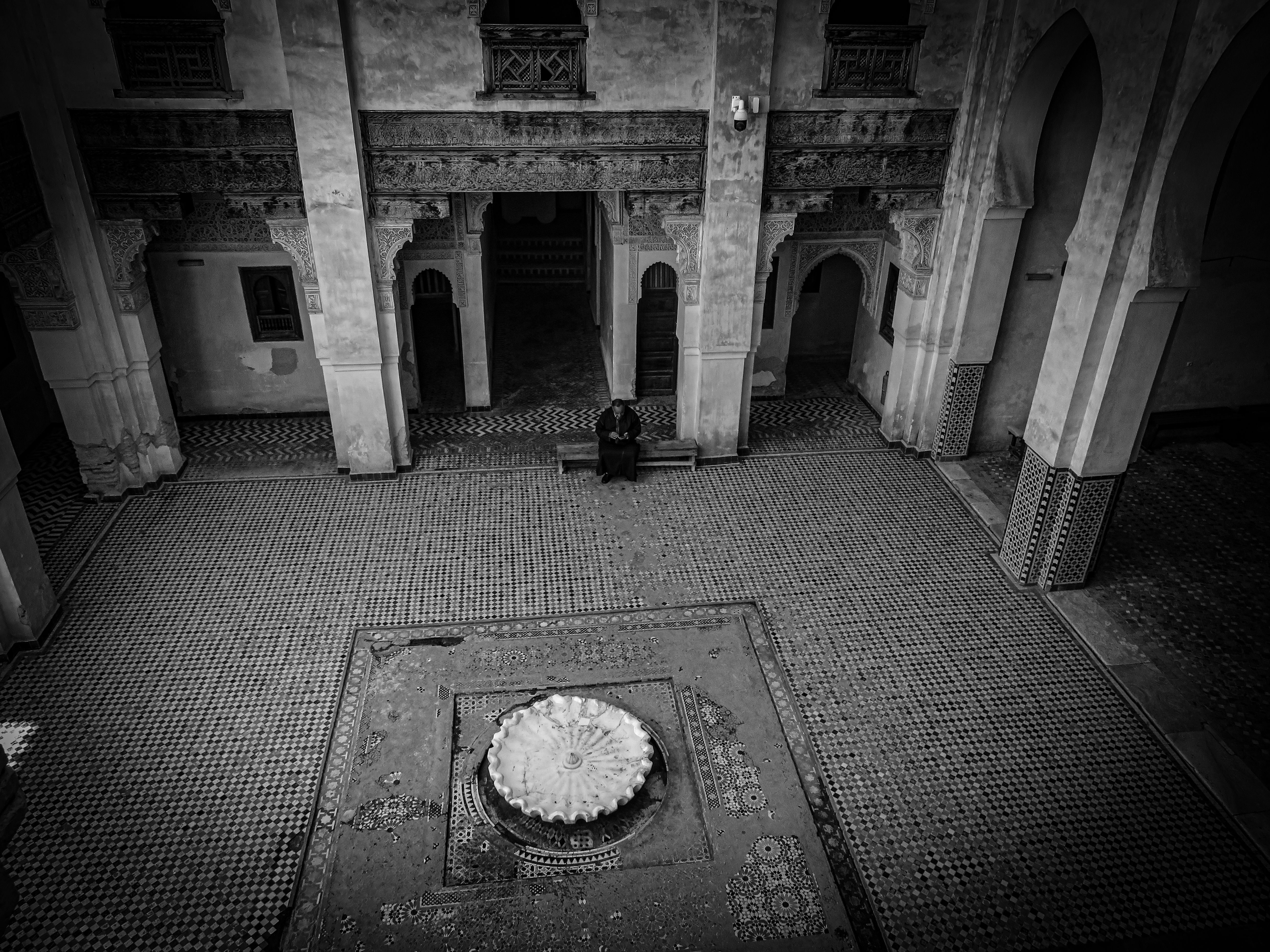 Black and white photo of a historic courtyard in Fez, Morocco with intricate tile work and central fountain.