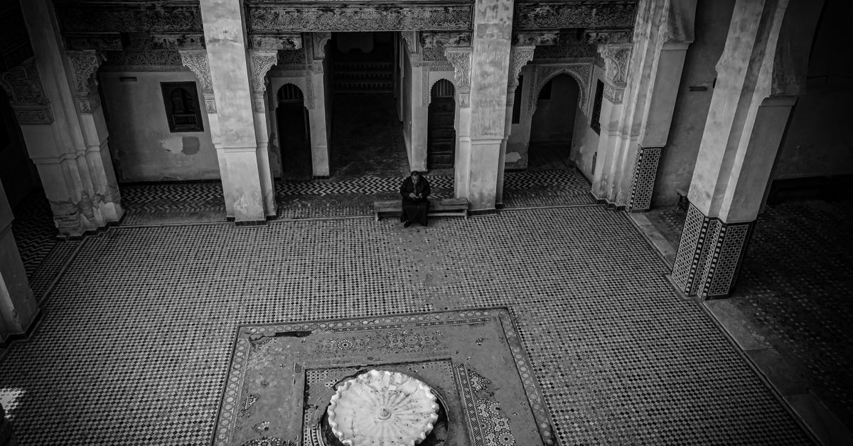 Black and white photo of a historic courtyard in Fez, Morocco with intricate tile work and central fountain.