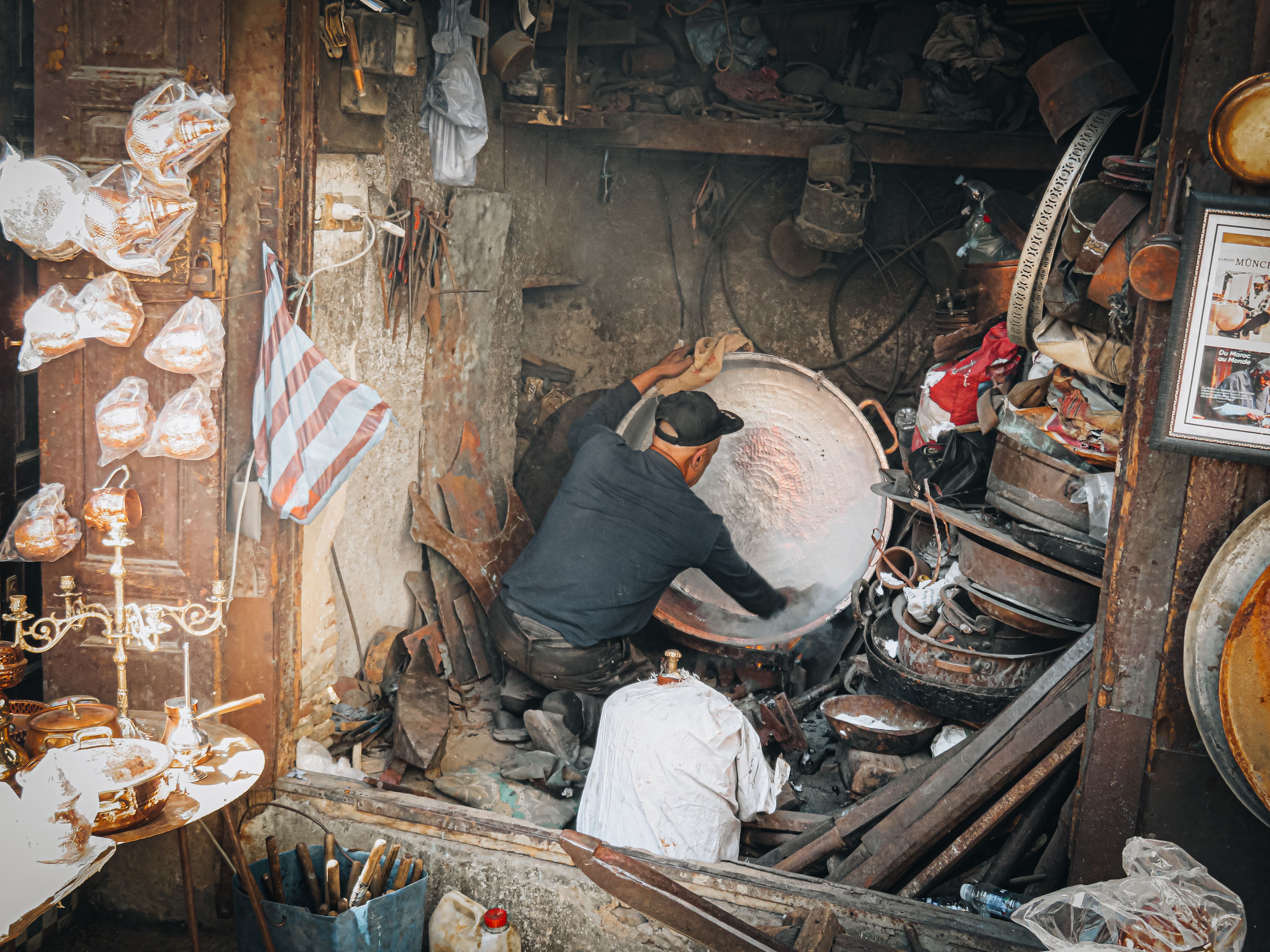 A skilled artisan works on metalware in a bustling Fez workshop, showcasing traditional Moroccan craftsmanship.