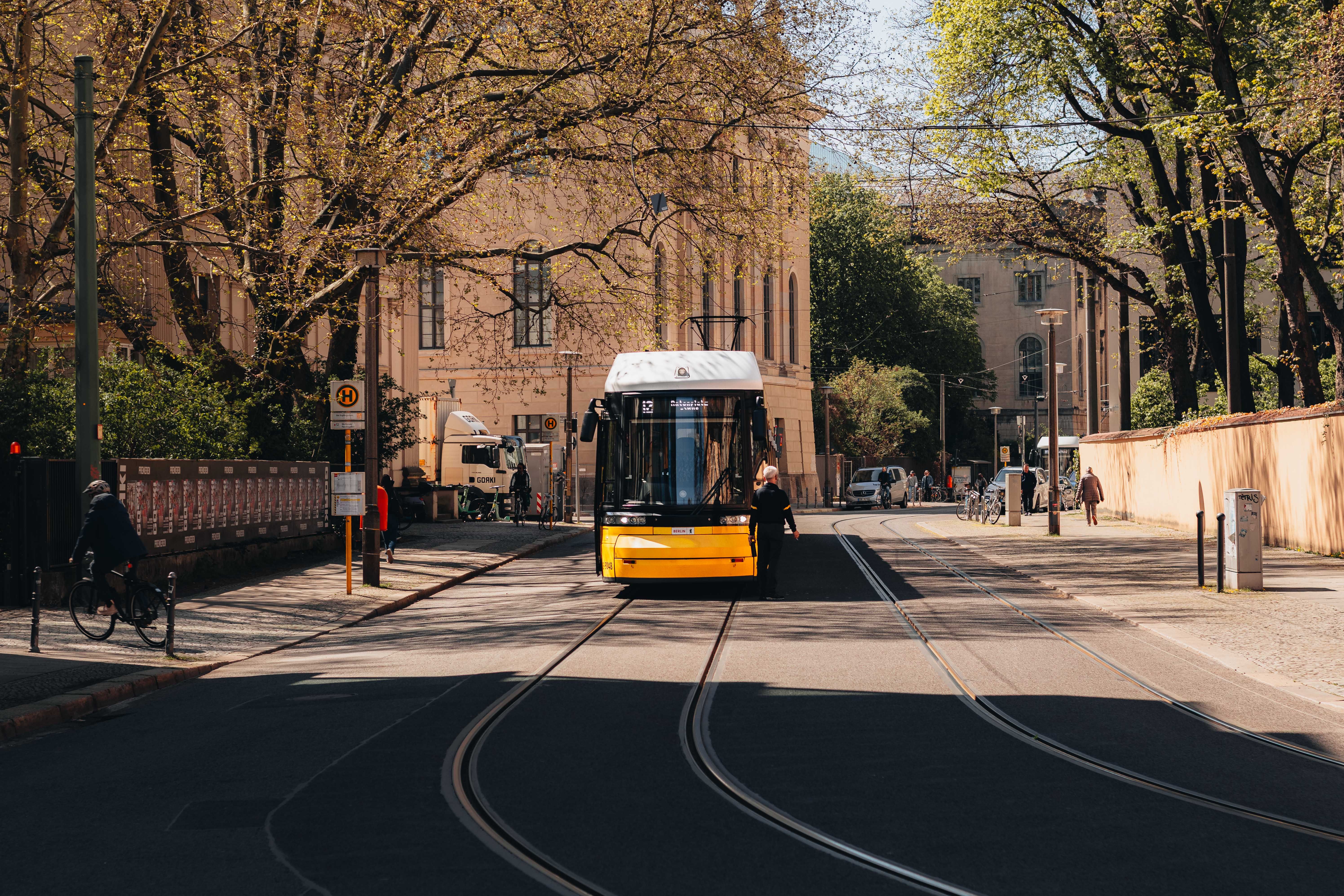 A vibrant yellow tram travels down a tree-lined street in Berlin on a sunny spring day.