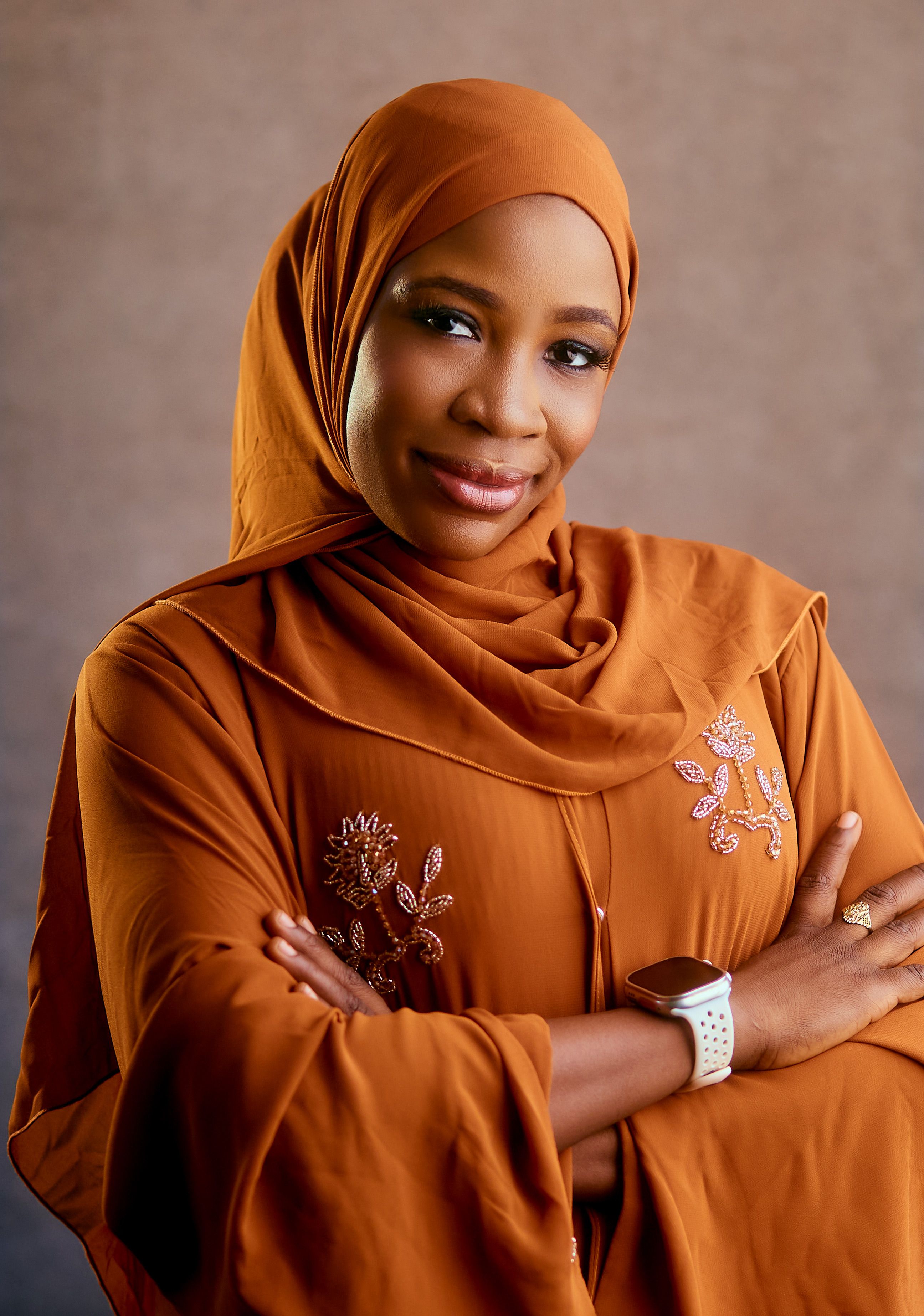 Confident woman wearing an orange hijab and embroidered dress with a watch.