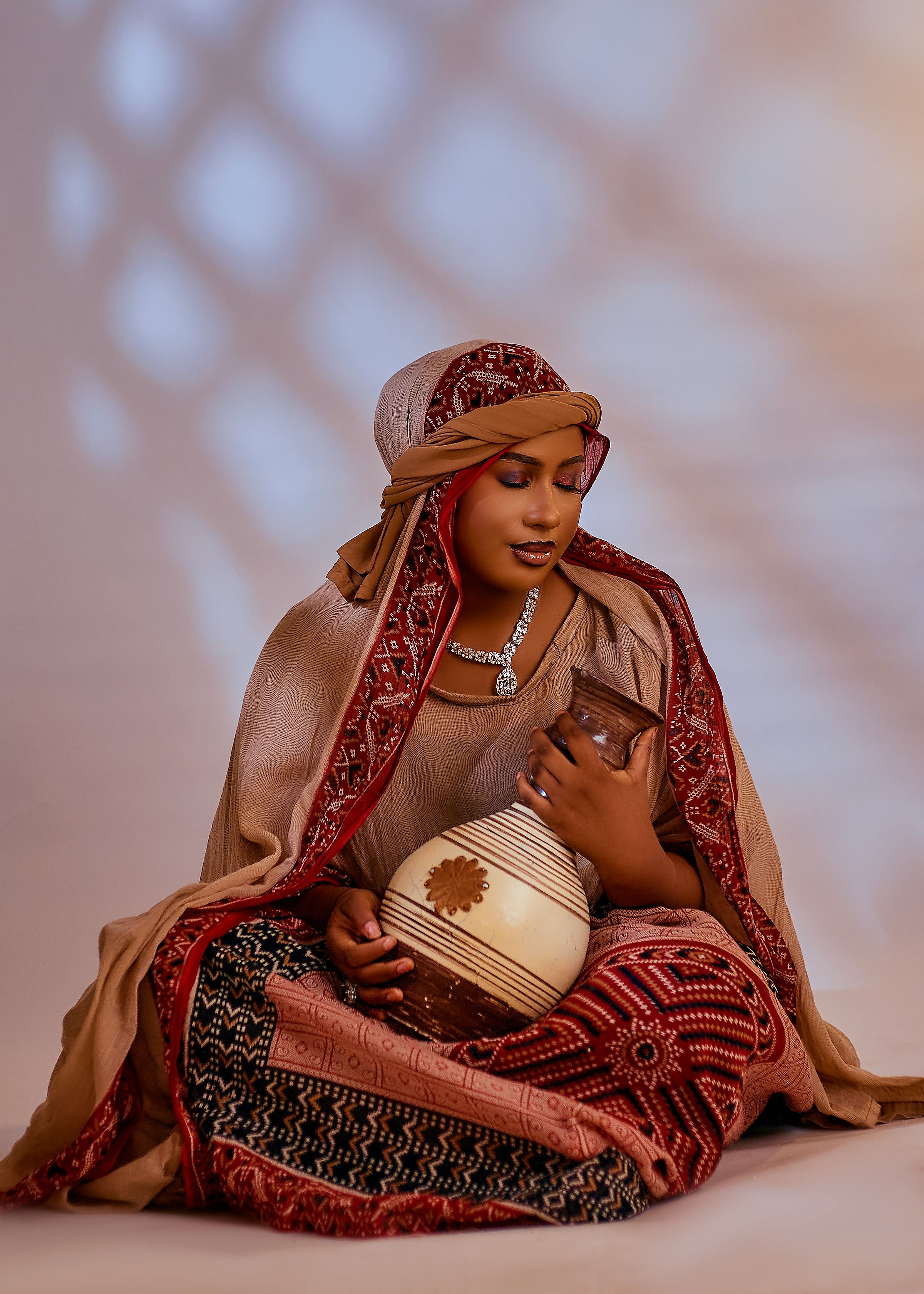Woman in traditional attire holding pottery against artistic background.
