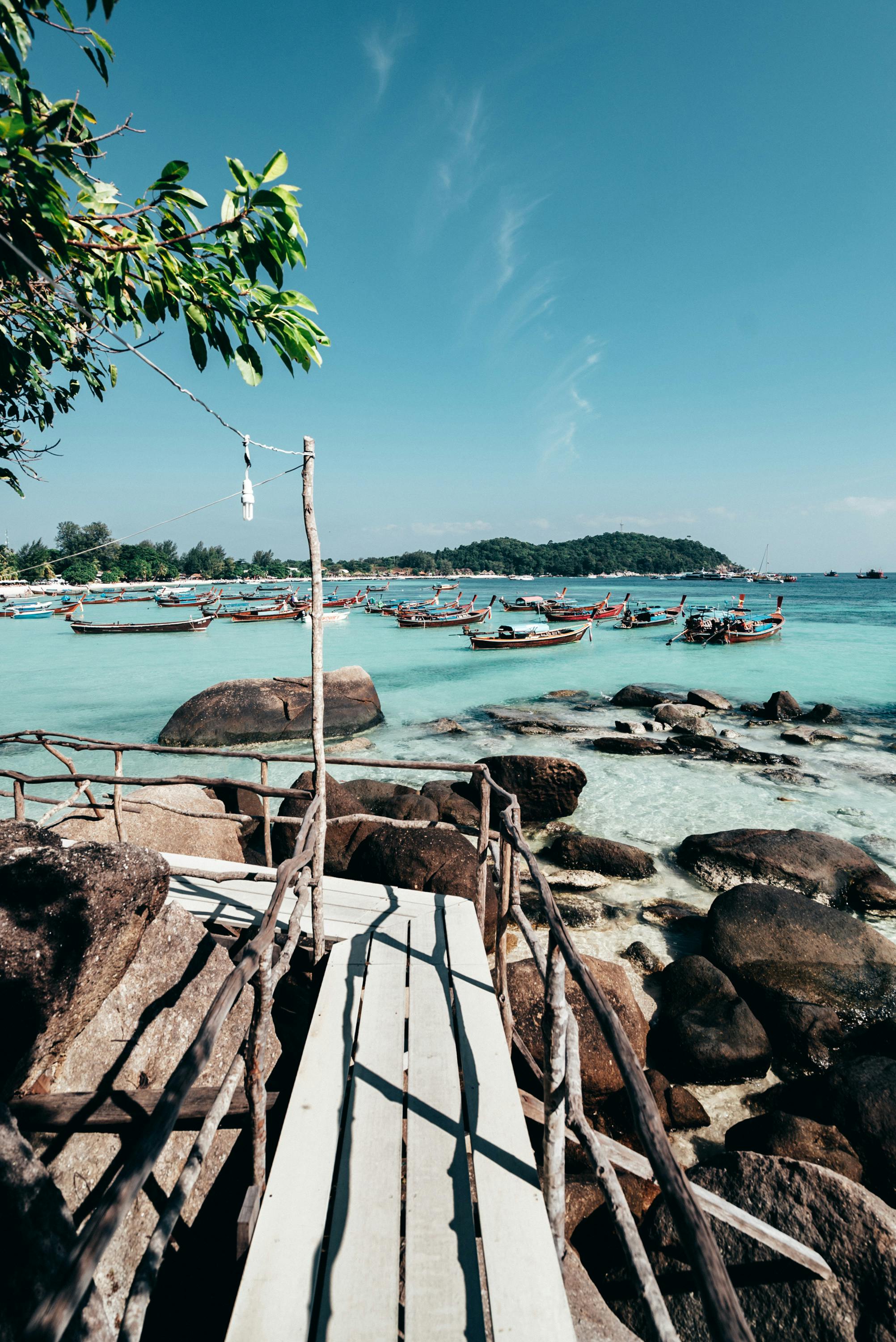 Serene view of wooden boats on clear water along a rocky Thai beach.