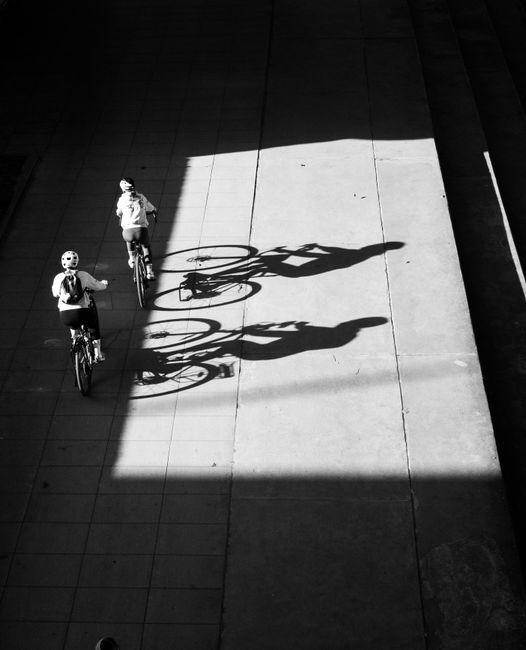 Aerial shot of two cyclists with dramatic shadows on a city street in black and white.
