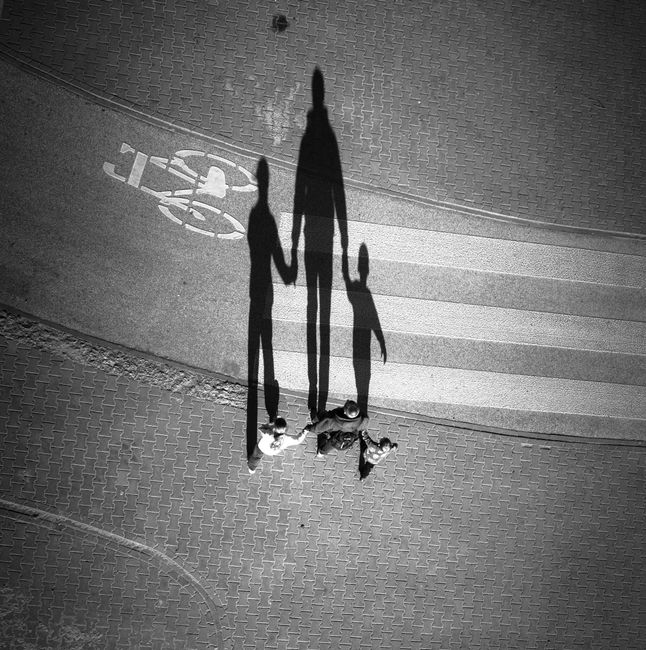 Artistic black and white aerial photo capturing a family's shadow crossing a paved street.