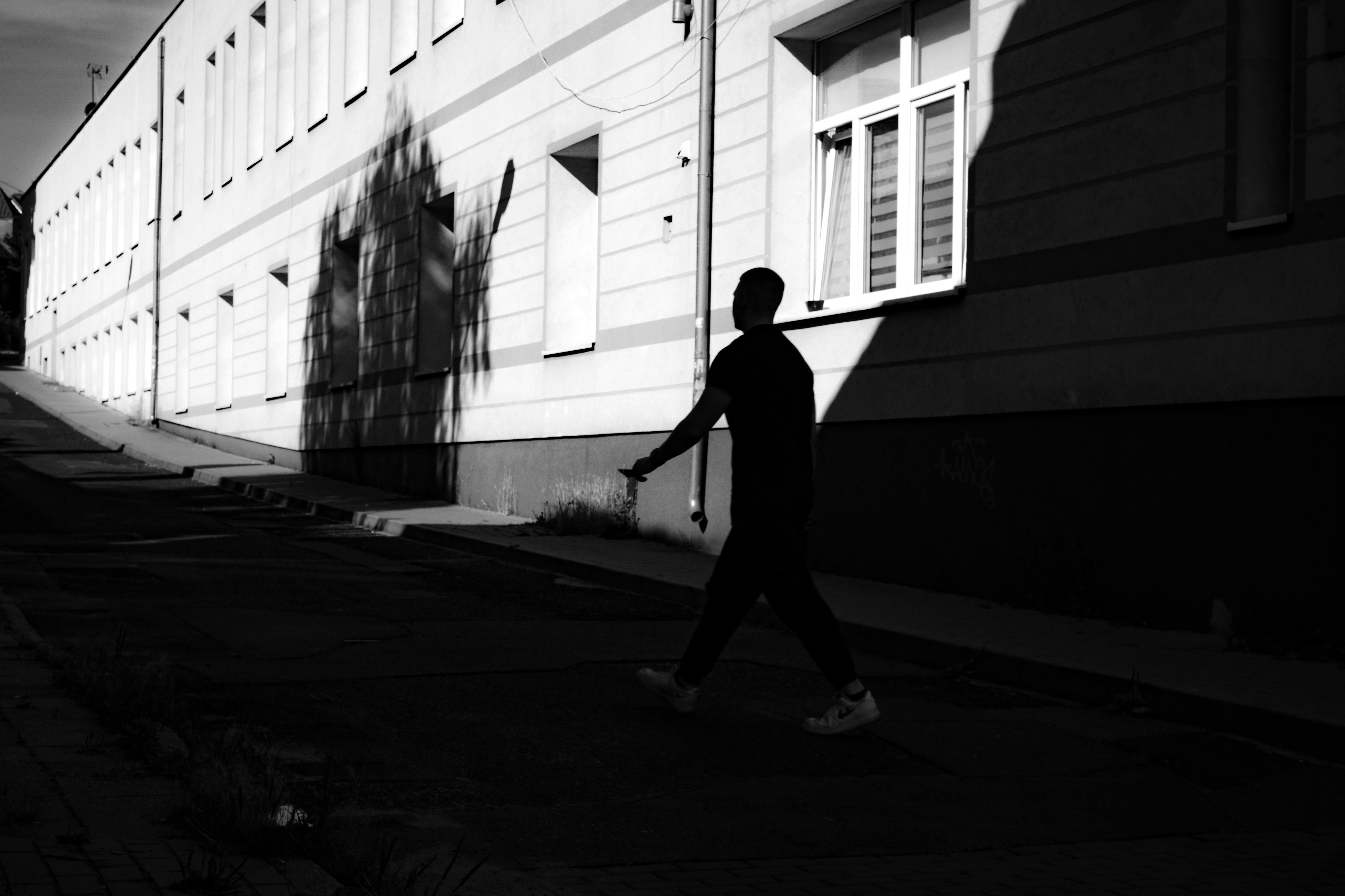 Black and white photo of a silhouette walking along a city street shadowed by a building.
