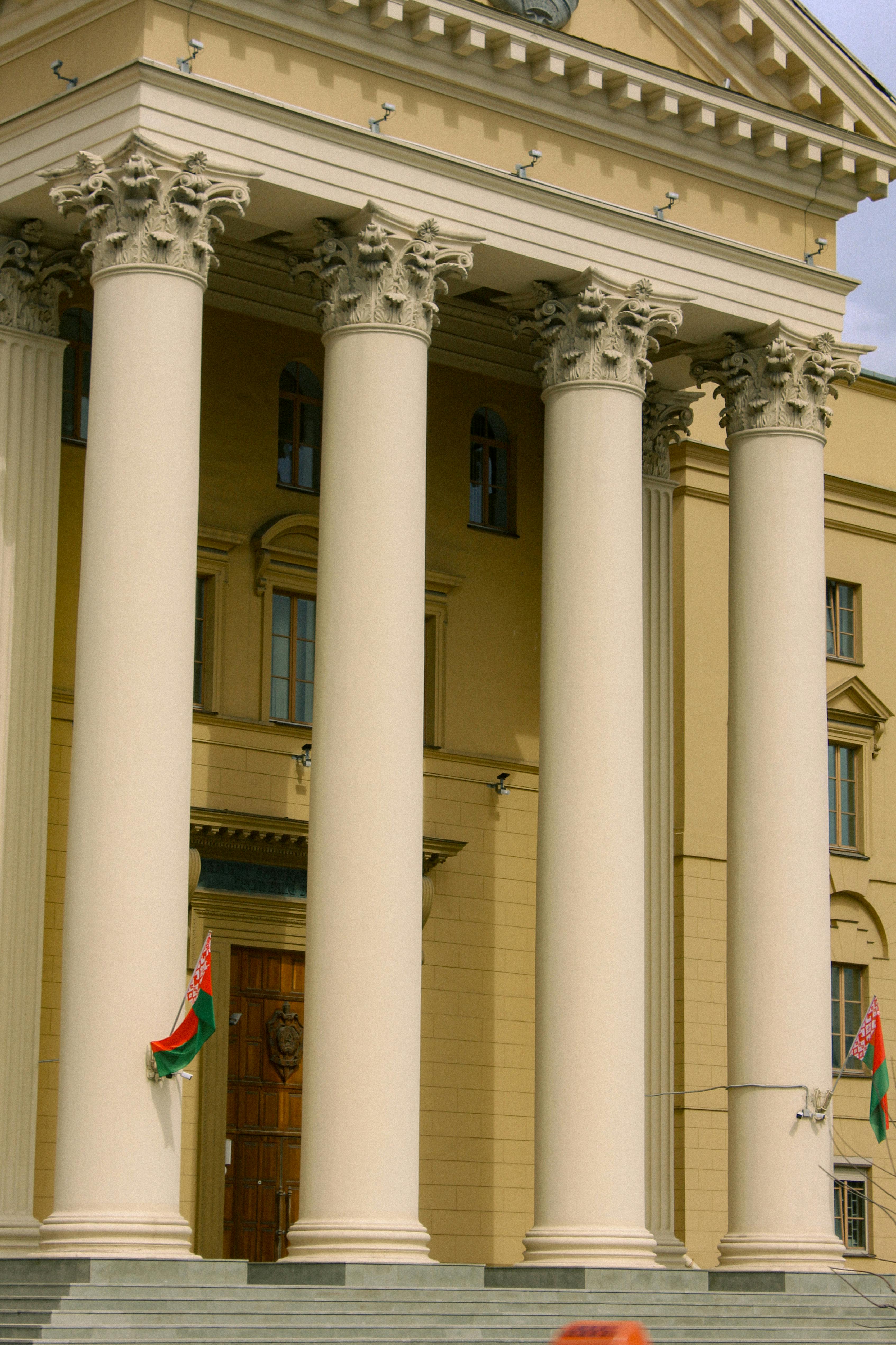 Imposing neoclassical facade with Corinthian columns and Belarusian flags.