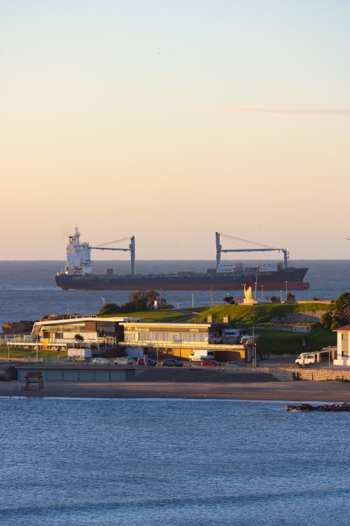 Free A cargo ship sails near the coastal cityscape of Mar del Plata at sunset. Stock Photo