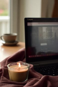 A warm and cozy workspace featuring a lit candle beside a laptop, creating a relaxing ambiance.