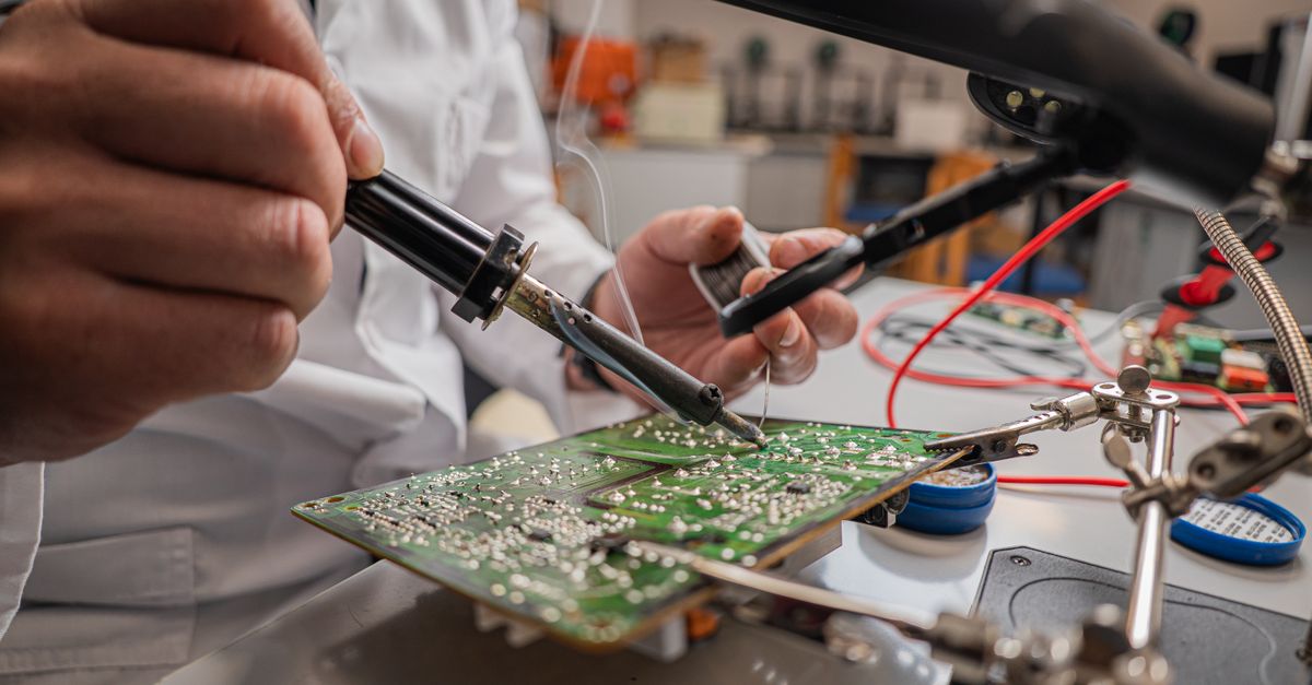 A skilled technician soldering electronic components on a green circuit board in a laboratory.