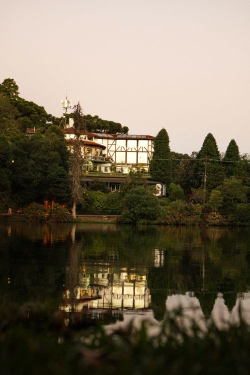 Free Charming lakeside building reflecting at dusk, surrounded by lush greenery and tranquil waters. Stock Photo