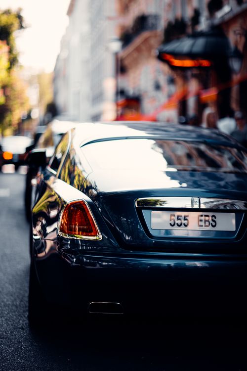 Free A sleek luxury car parked on a bustling European street, captured in soft focus with vibrant colors. Stock Photo