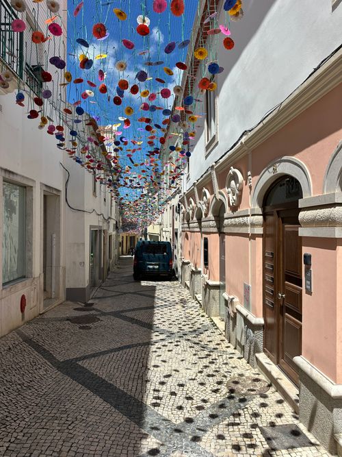 Free Colorful street decorations hanging above a cobblestone alleyway in Torres Vedras, Portugal. Stock Photo