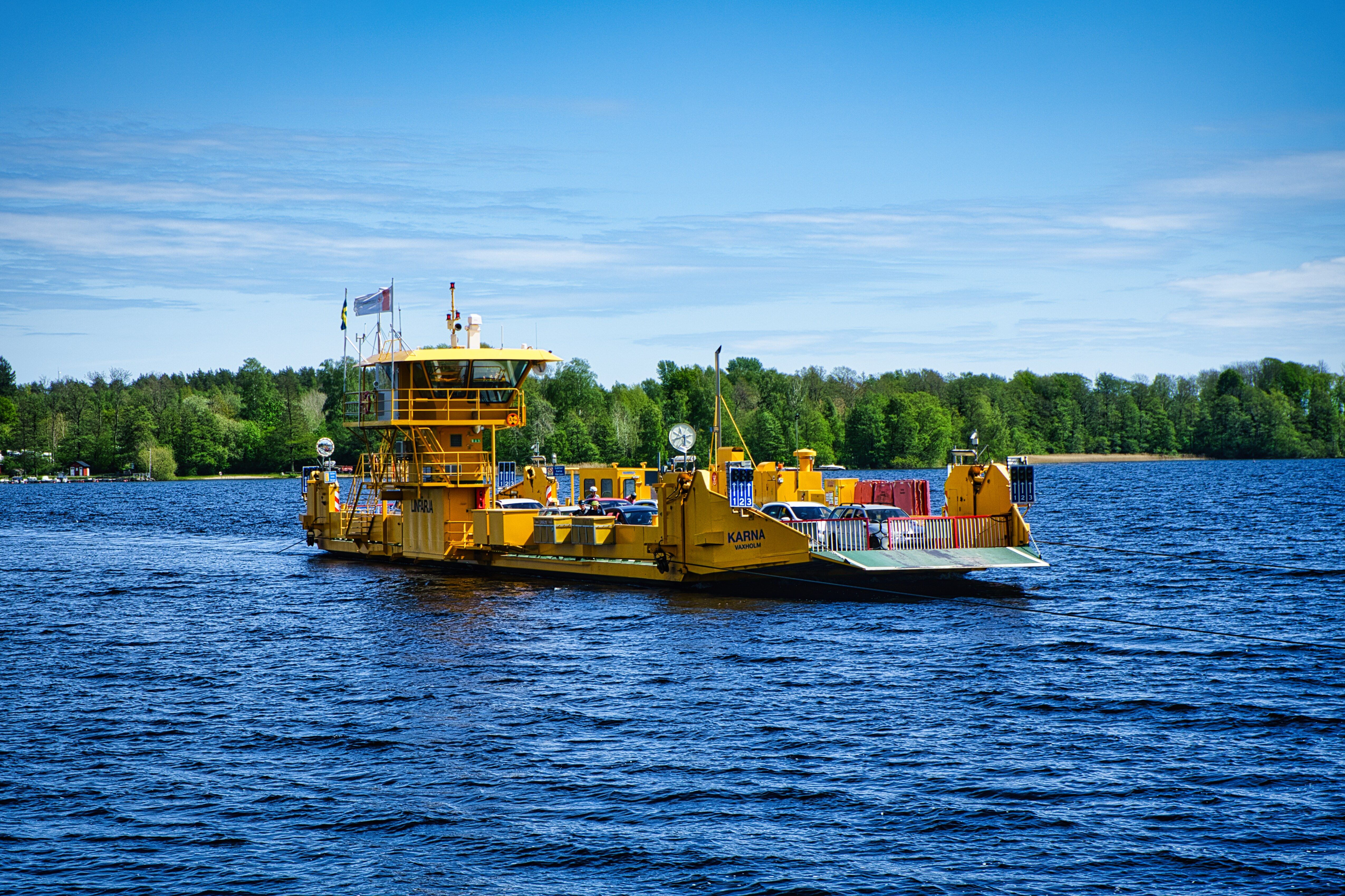 Bright yellow ferry crossing Ivö Lake in Skåne, Sweden under clear blue skies.