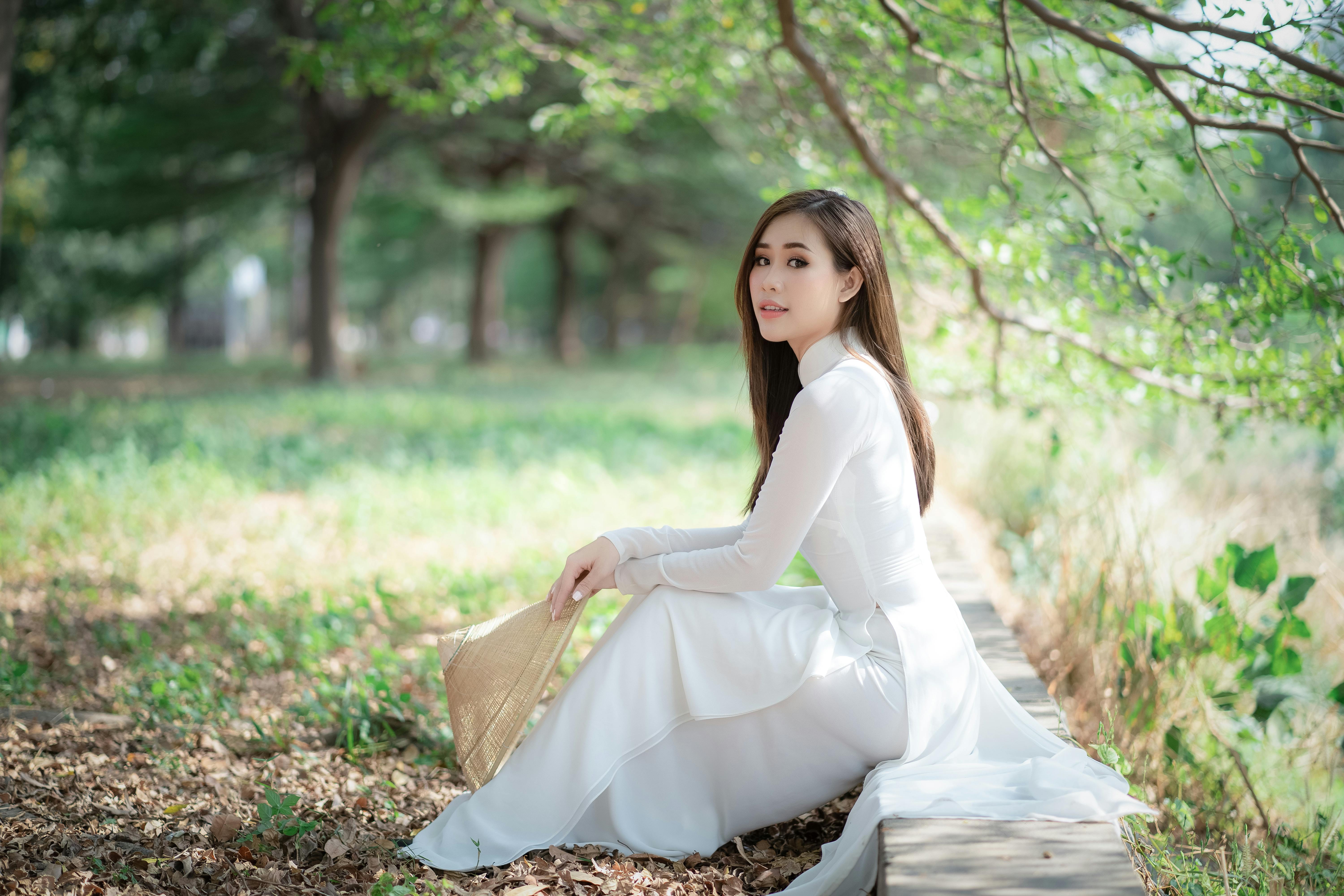 一名身穿白裙、头戴草帽的女子，静静地坐在绿色的公园里