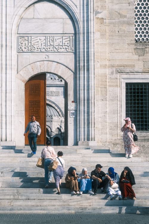Free People sit and socialize on steps of an Ottoman-style building entrance on a sunny day. Stock Photo