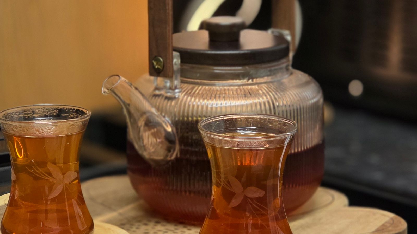 A glass teapot and two glasses of tea on a wooden tray