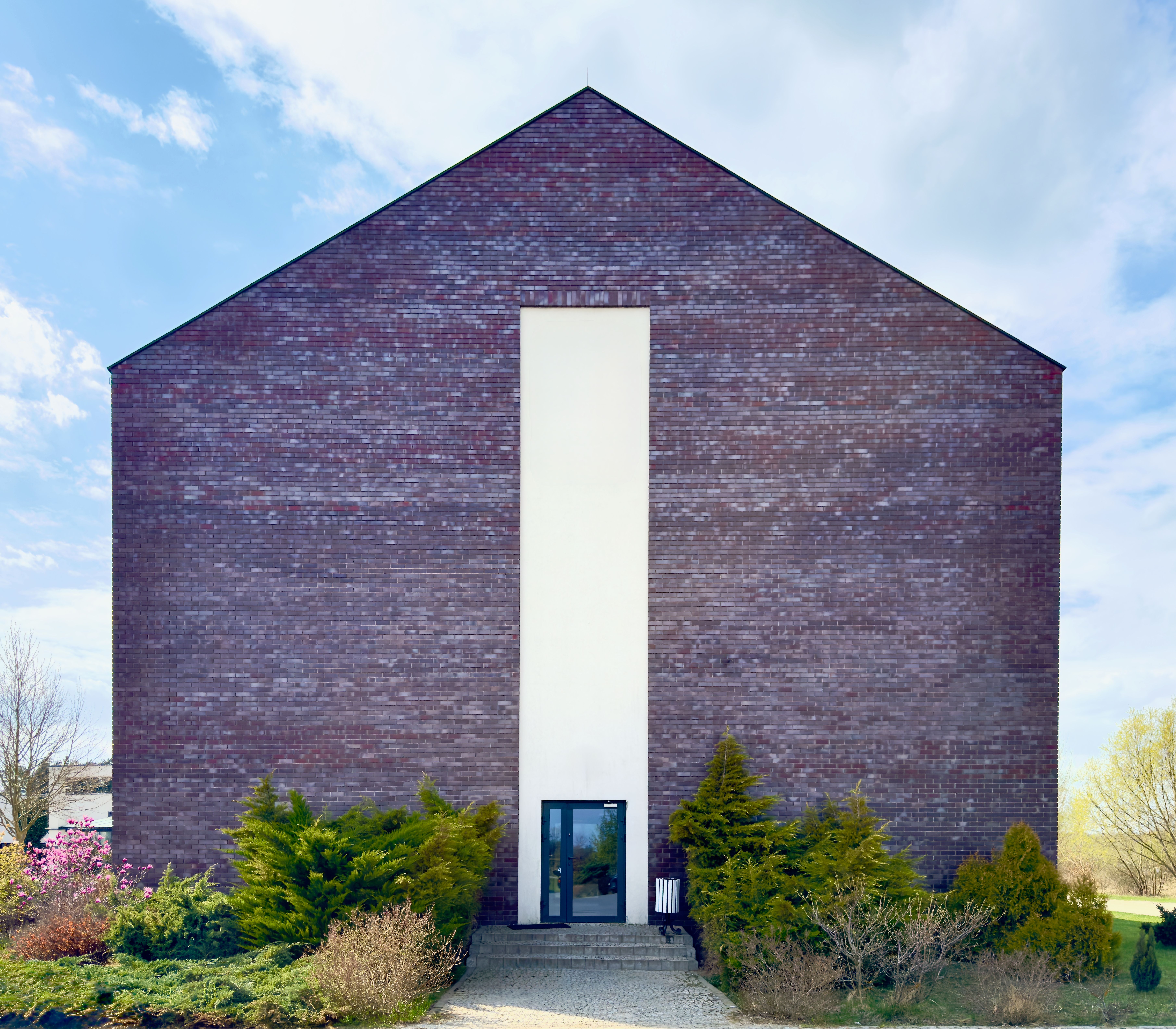 Minimalist brick building with symmetric design and lush greenery in Uniejów, Poland.