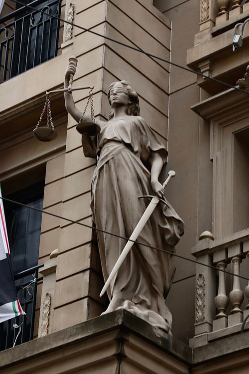 Free A stone statue of Lady Justice stands on the facade of a historic building, symbolizing law and order. Stock Photo
