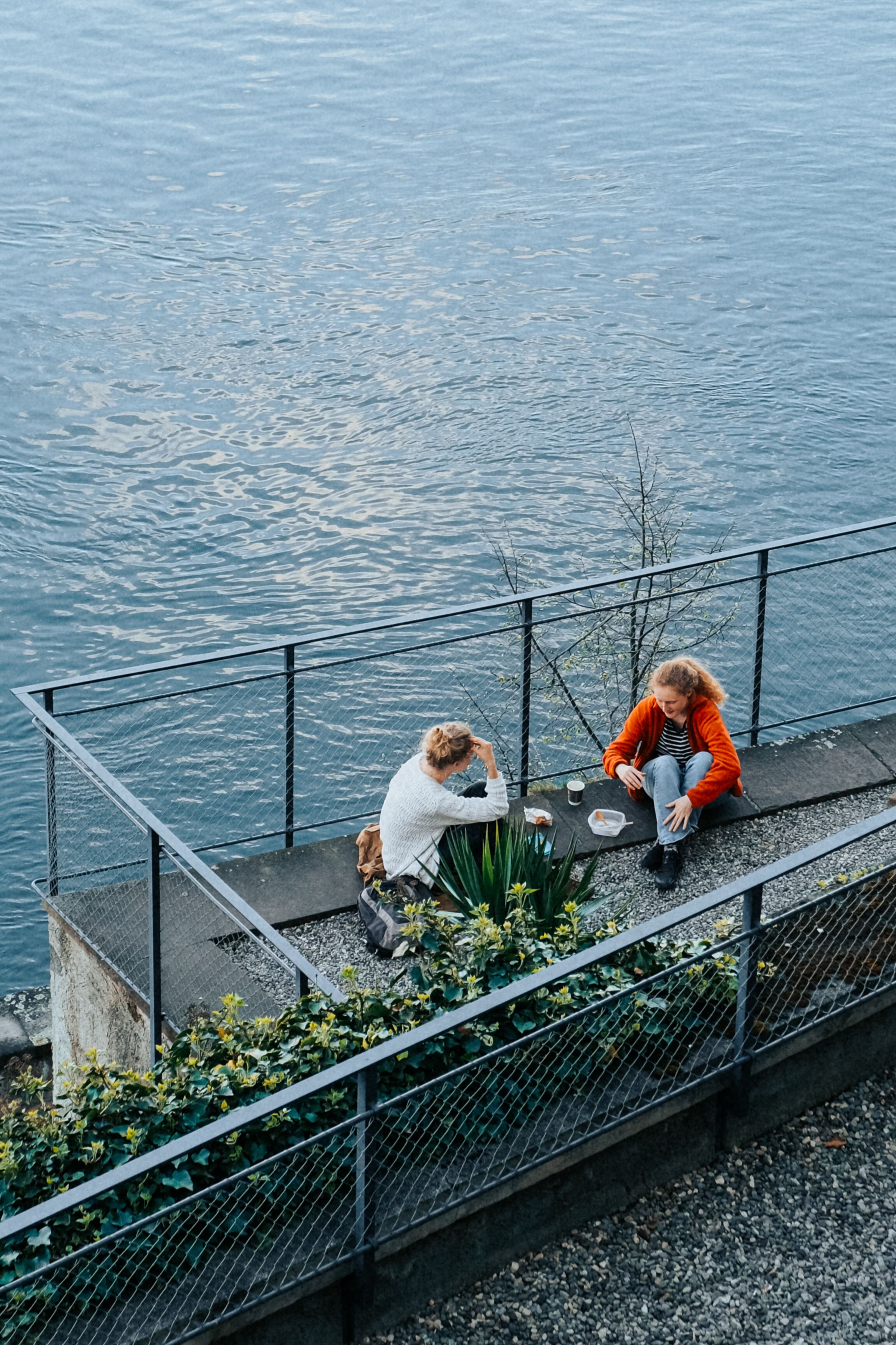 Two people enjoying a riverside chat in Basel, Switzerland, with a serene water view.