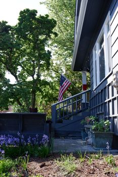 Charming blue house in Seattle with garden and American flag, surrounded by lush greenery.