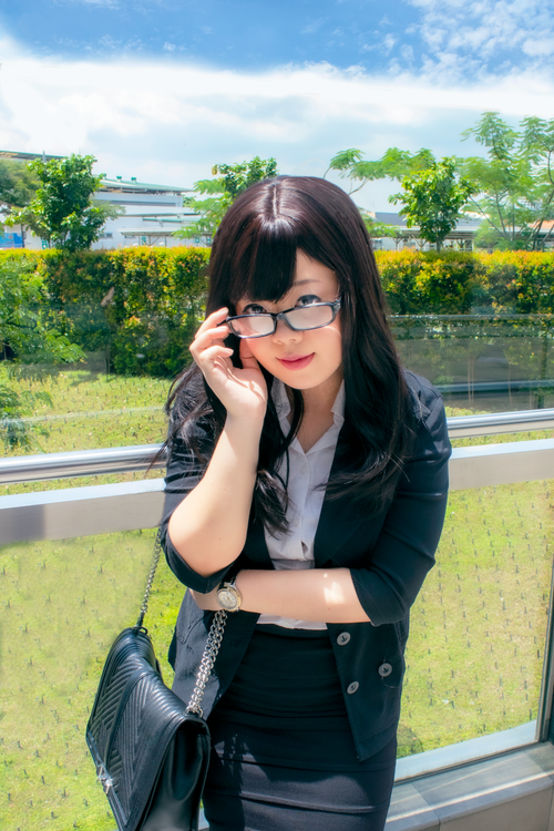 Free Confident woman with glasses and a black blazer standing outdoors with greenery. Stock Photo