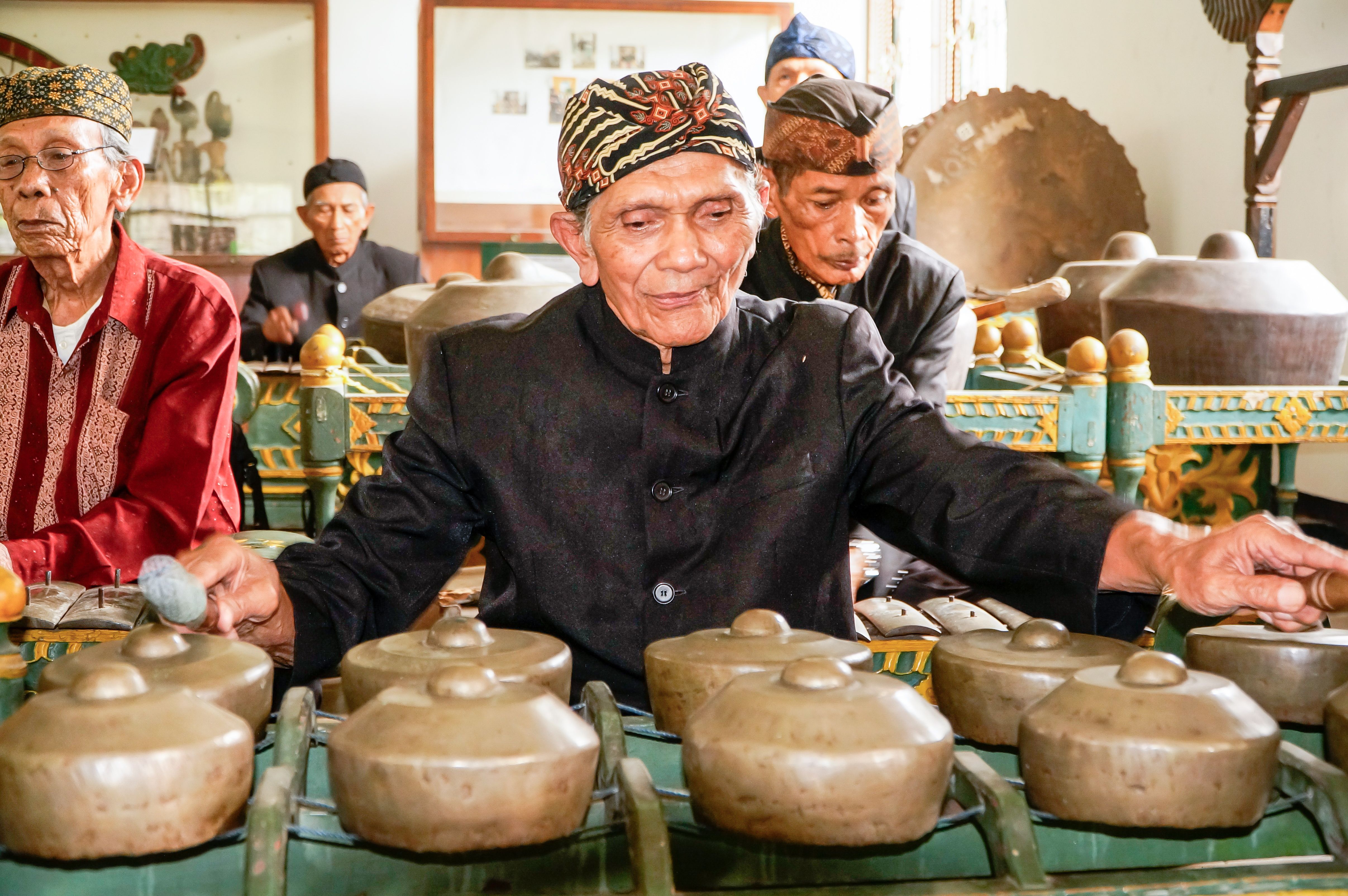 Senior musicians playing traditional Indonesian gamelan instruments indoors. Cultural heritage captured vividly.