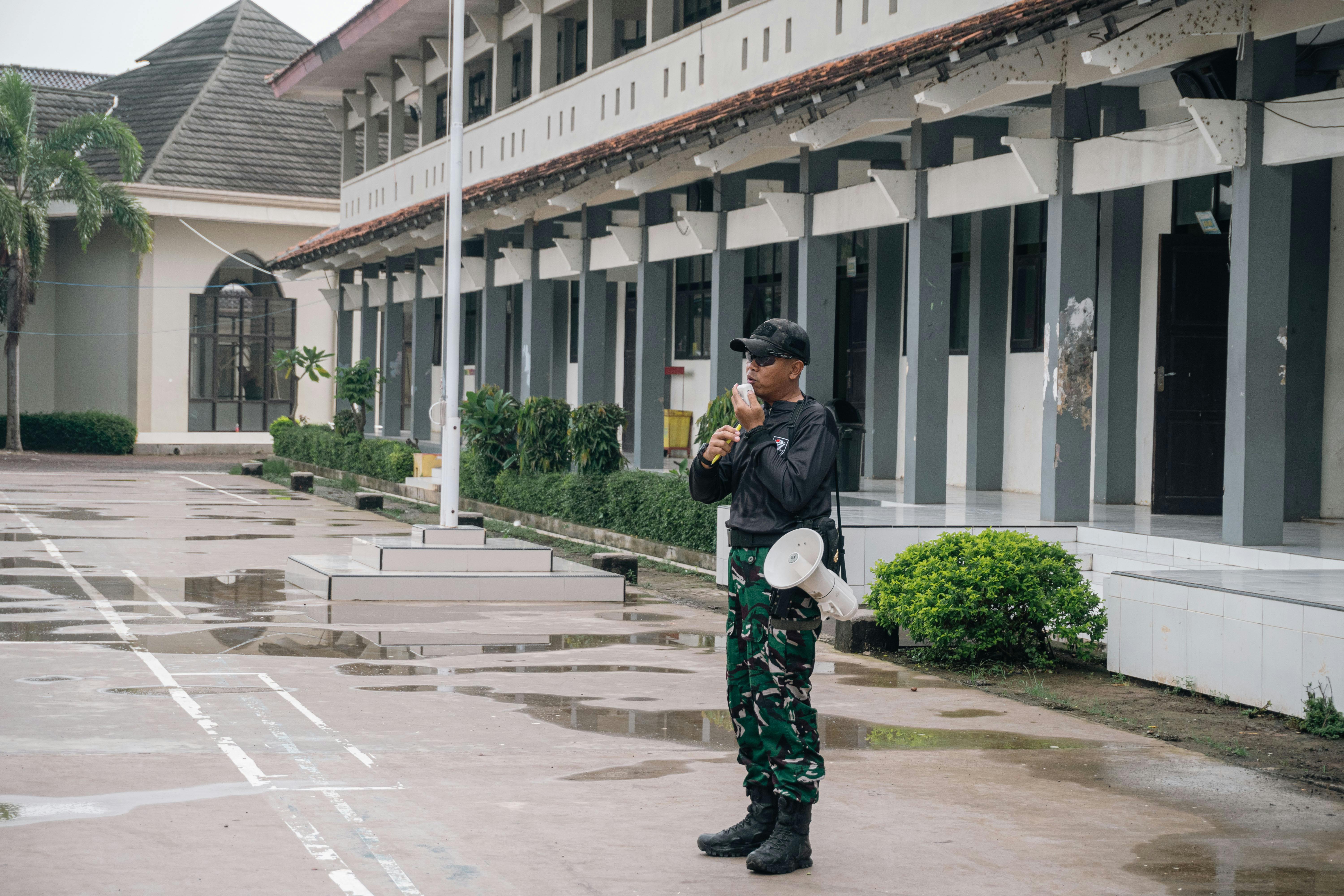 A security guard stands alert with a megaphone outside a building after rain.