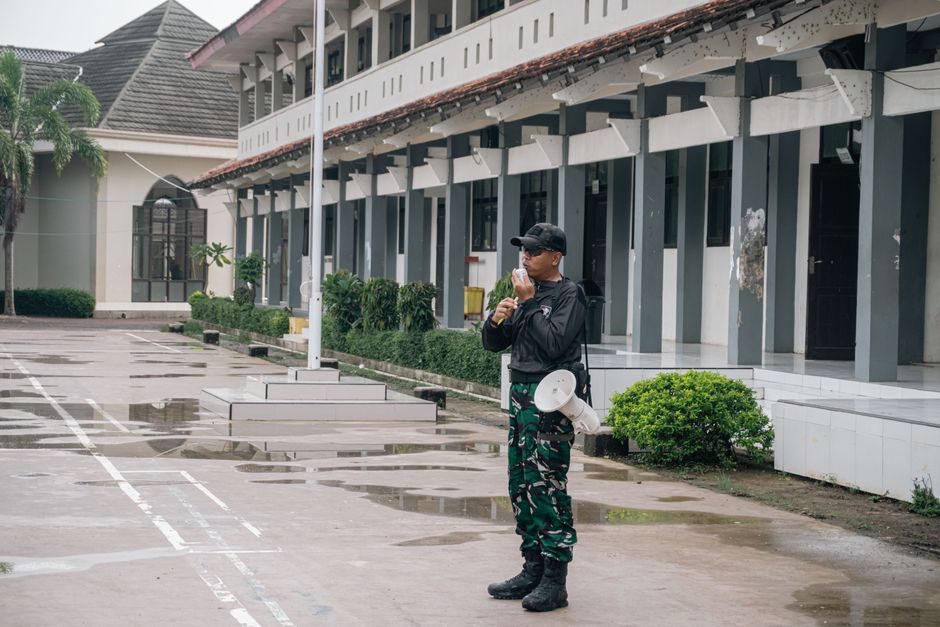 A security guard stands alert with a megaphone outside a building after rain. A security guard stands alert with a megaphone outside a building after rain.