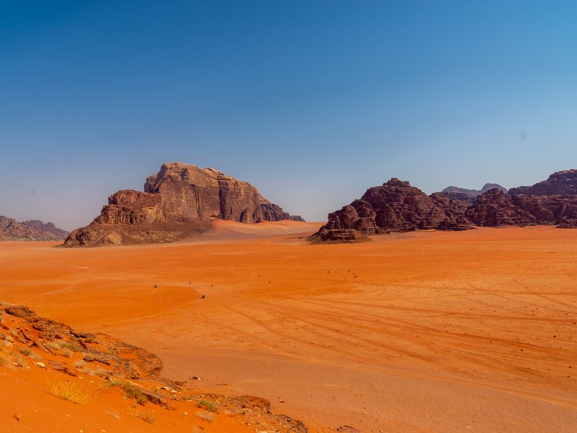 Red desert floor meeting towering rock formations in Wadi Rum