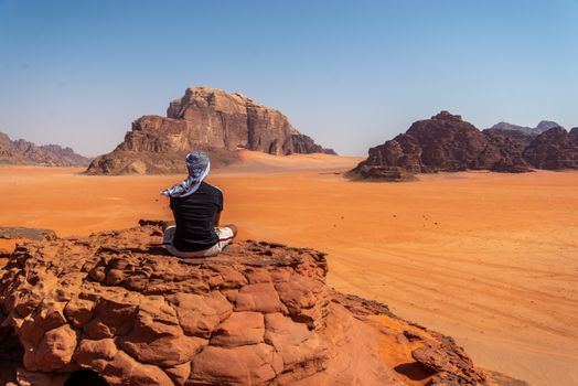 Solo traveler sitting on rocks and enjoying the vast landscape of Wadi Rum desert in Ürdün.