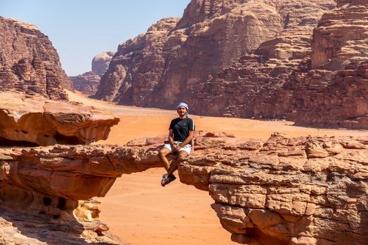 A person seated on a natural rock bridge in the Wadi Rum desert, showcasing stunning sandstone formations.