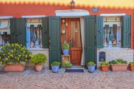 A vibrant house facade with green shutters and potted plants in a rustic setting.