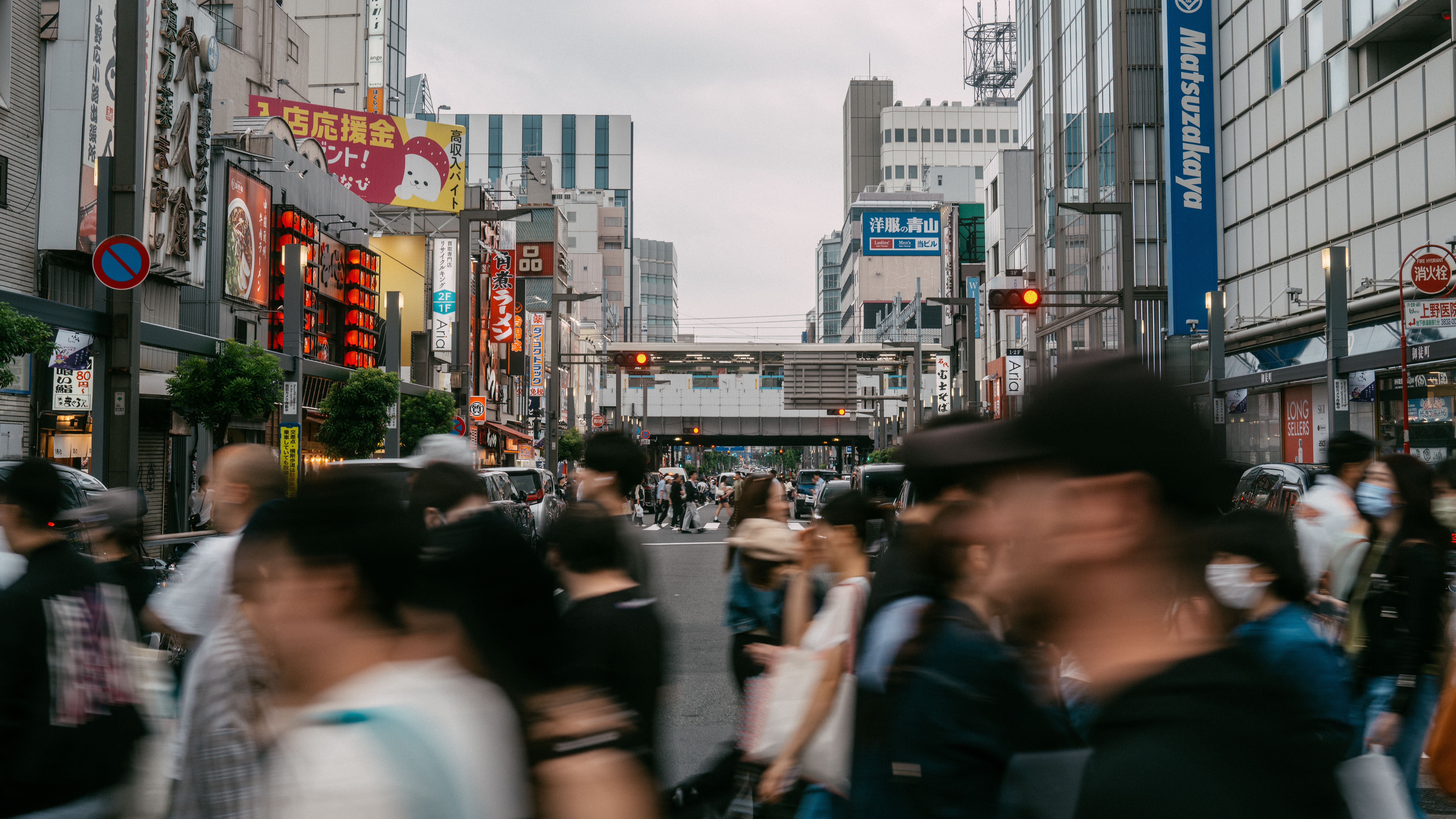 広告看板や建物に囲まれた、賑やかな東京の通りを横断する歩行者たち。