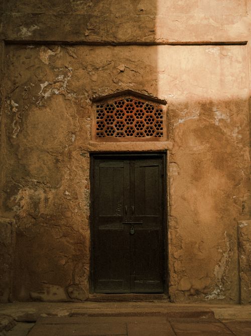 Free A rustic wooden door with a vintage lattice vent set in an aged textured wall, capturing historical architecture. Stock Photo