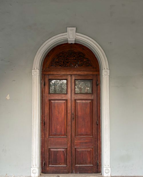 Free A beautifully crafted wooden door with an arched frame and intricate woodwork in a classic architectural style. Stock Photo