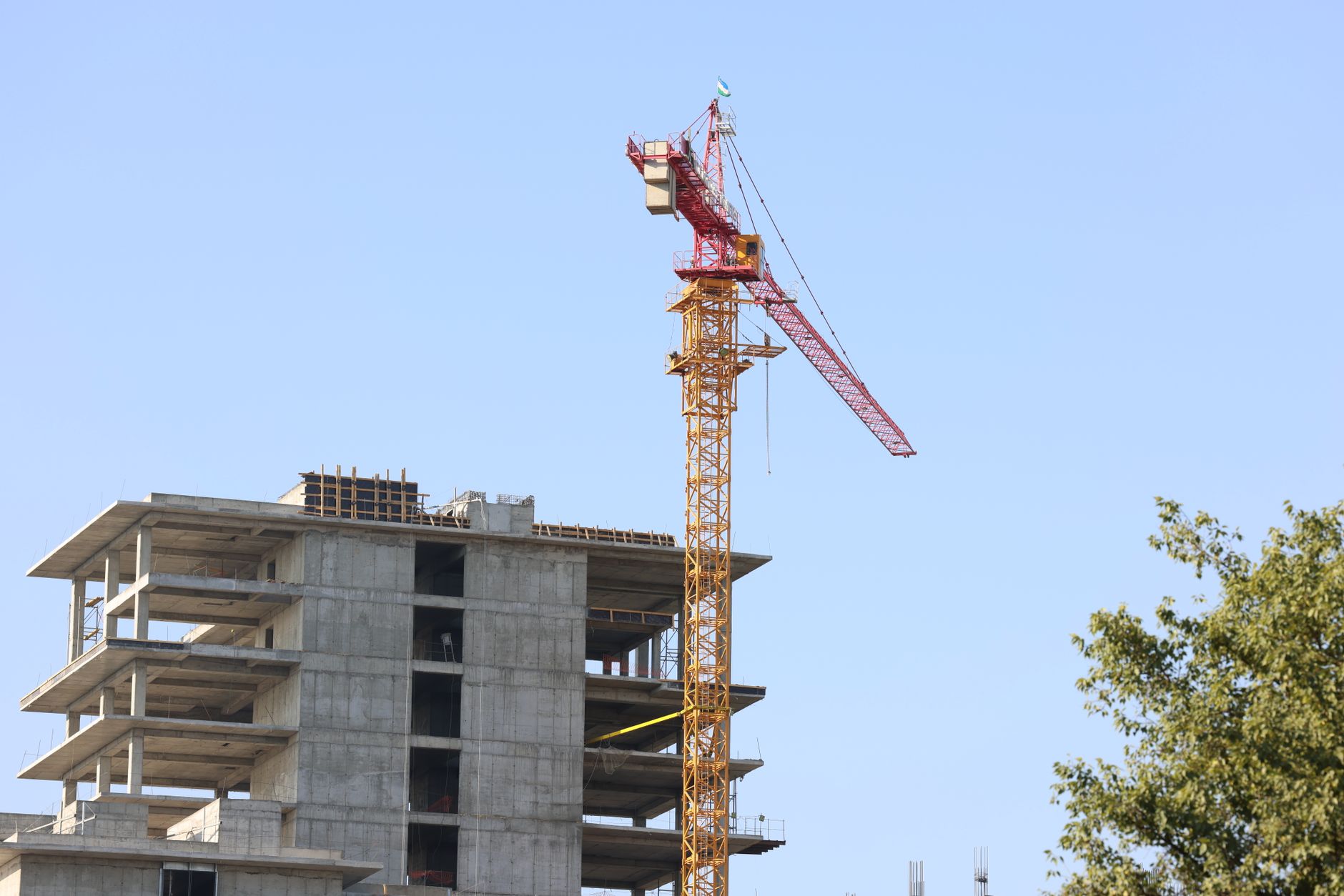 High-rise building under construction with crane in Oʻzbekiston cityscape.