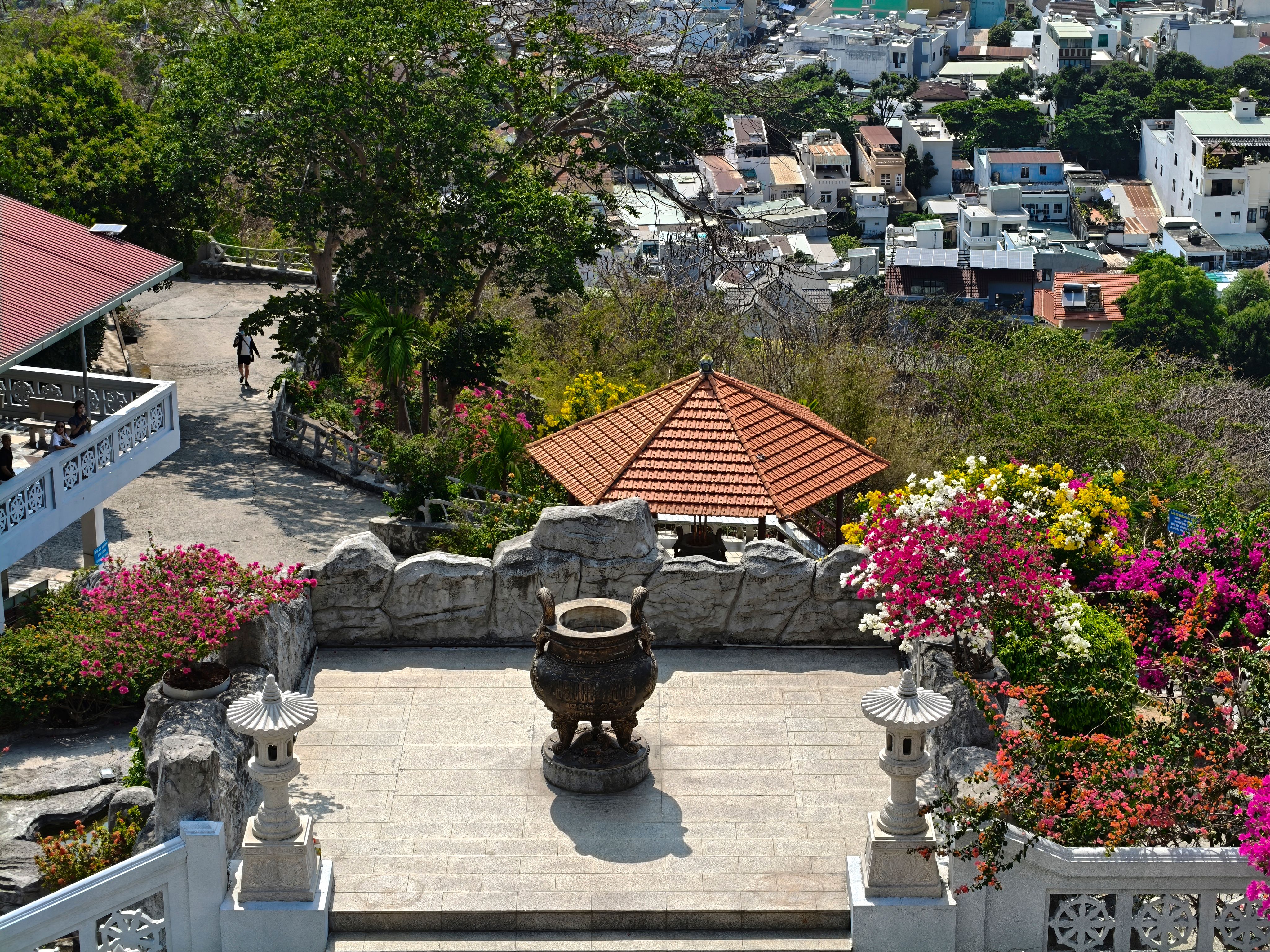 Overview of a hilltop temple with lush gardens and cityscape in the background.