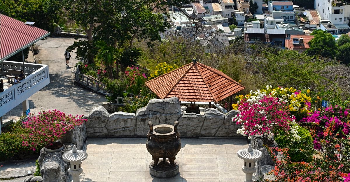 Overview of a hilltop temple with lush gardens and cityscape in the background.