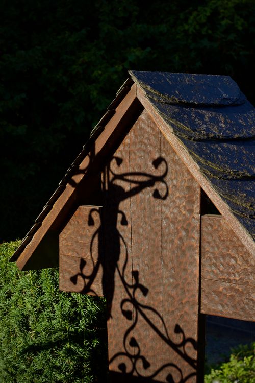 Free A decorative shadow cast by wrought iron on a textured wooden roof with lush greenery. Stock Photo