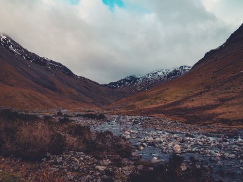 Free A picturesque view of a mountain valley with a flowing river under a cloudy sky. Stock Photo