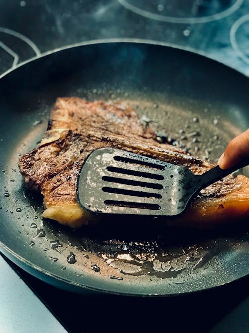 A Hand Frying a Meat on Black Pan