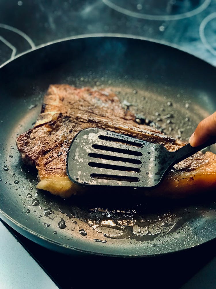 A Hand Frying A Meat On Black Pan