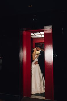 A newlywed couple shares a romantic kiss in a modern elevator setting.