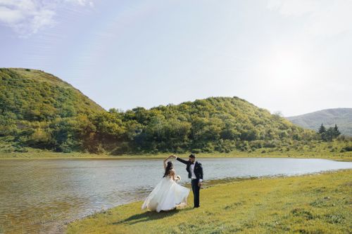 Free Bride and groom dancing elegantly by a tranquil lakeside on a sunny day. Stock Photo