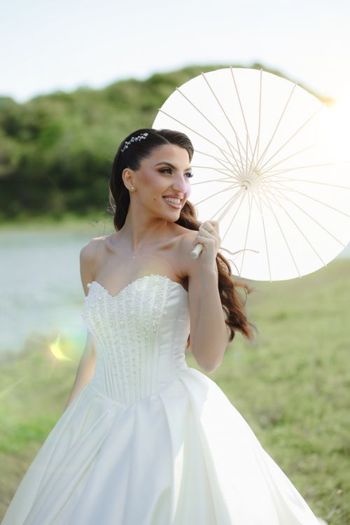 Free Bride in wedding dress holding parasol outdoors by a lake. Stock Photo