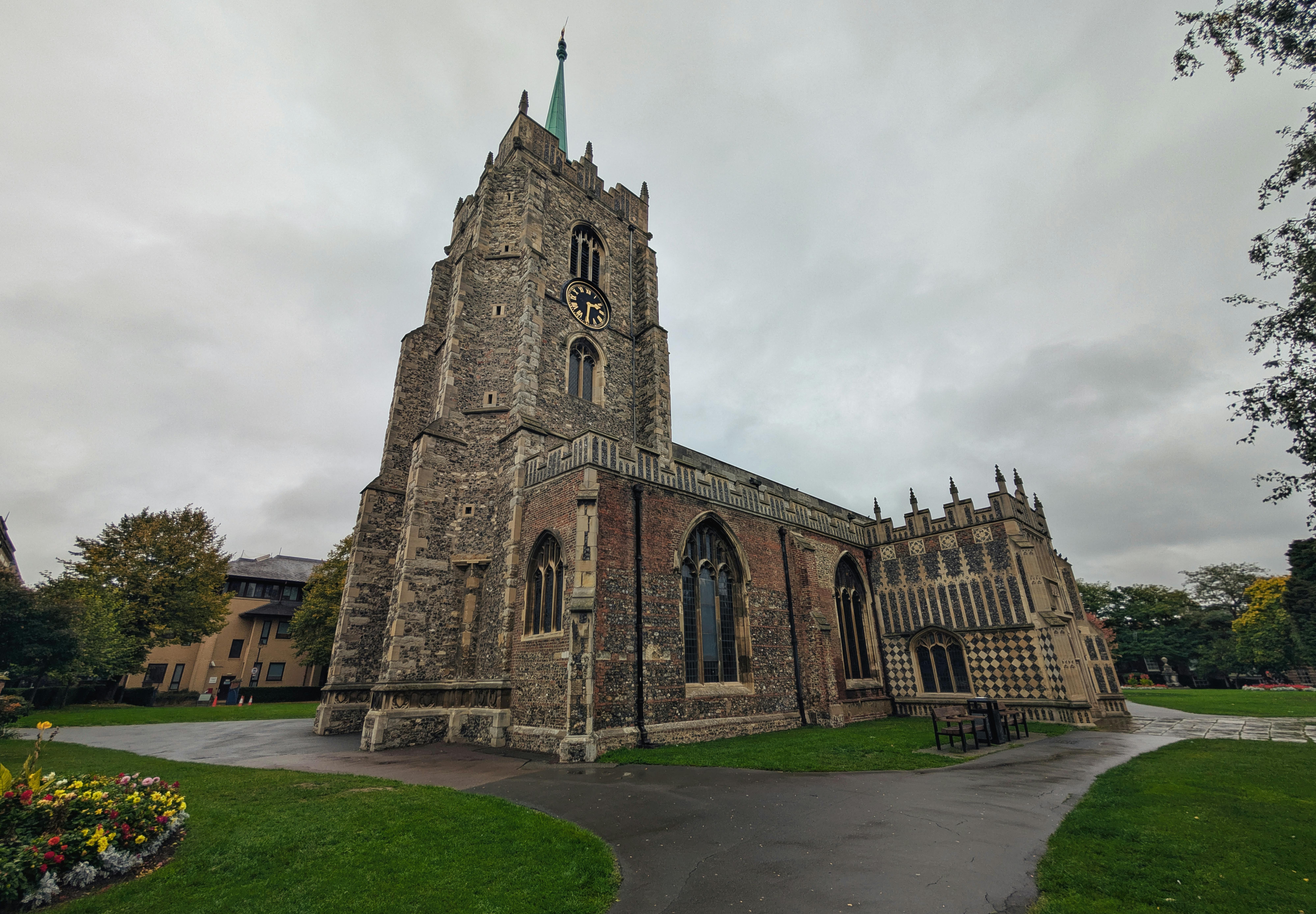 A low-angle view of Chelmsford Cathedral with its clock tower and stained glass windows under a cloudy sky.