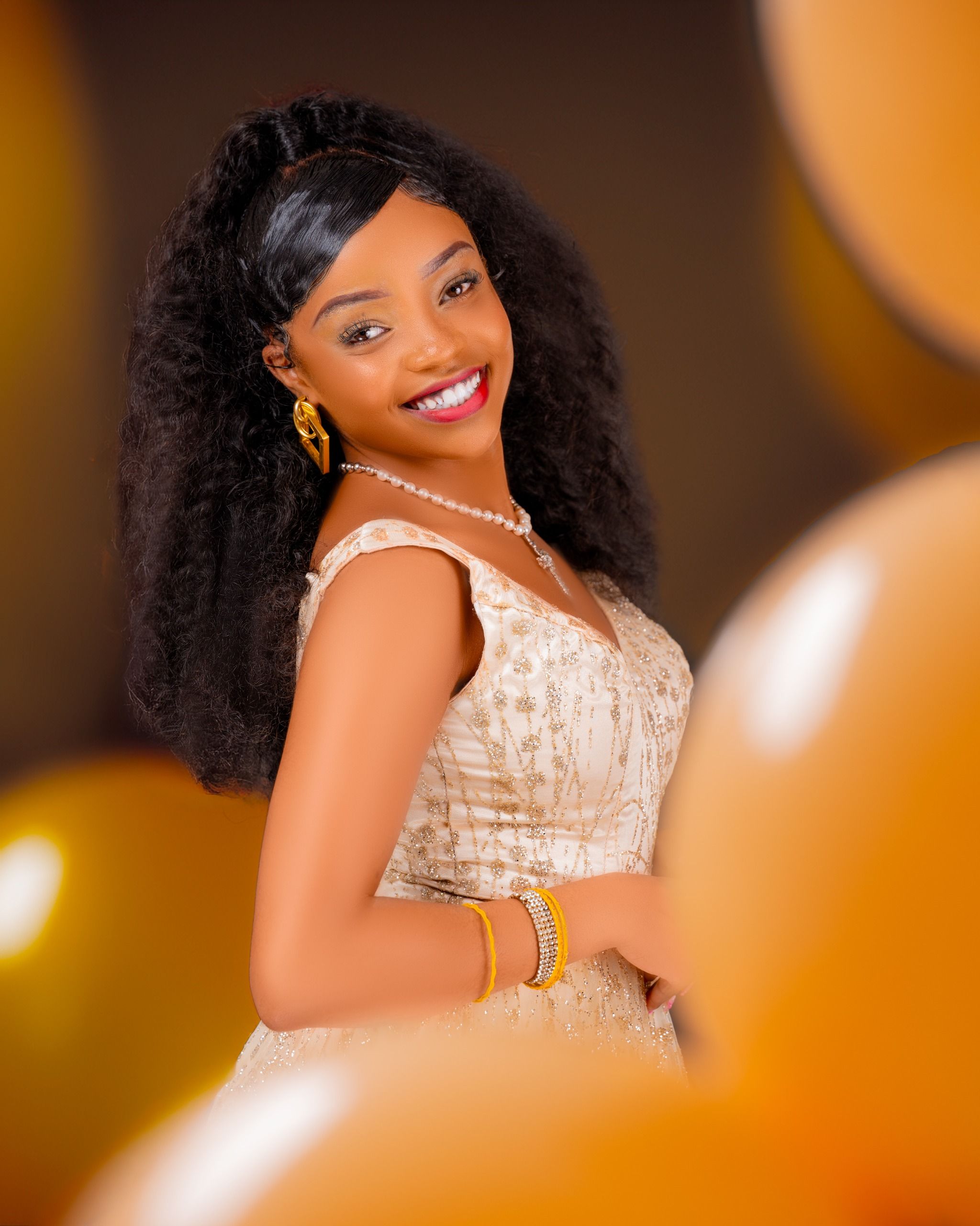 Smiling woman in elegant dress surrounded by golden balloons at a celebration.