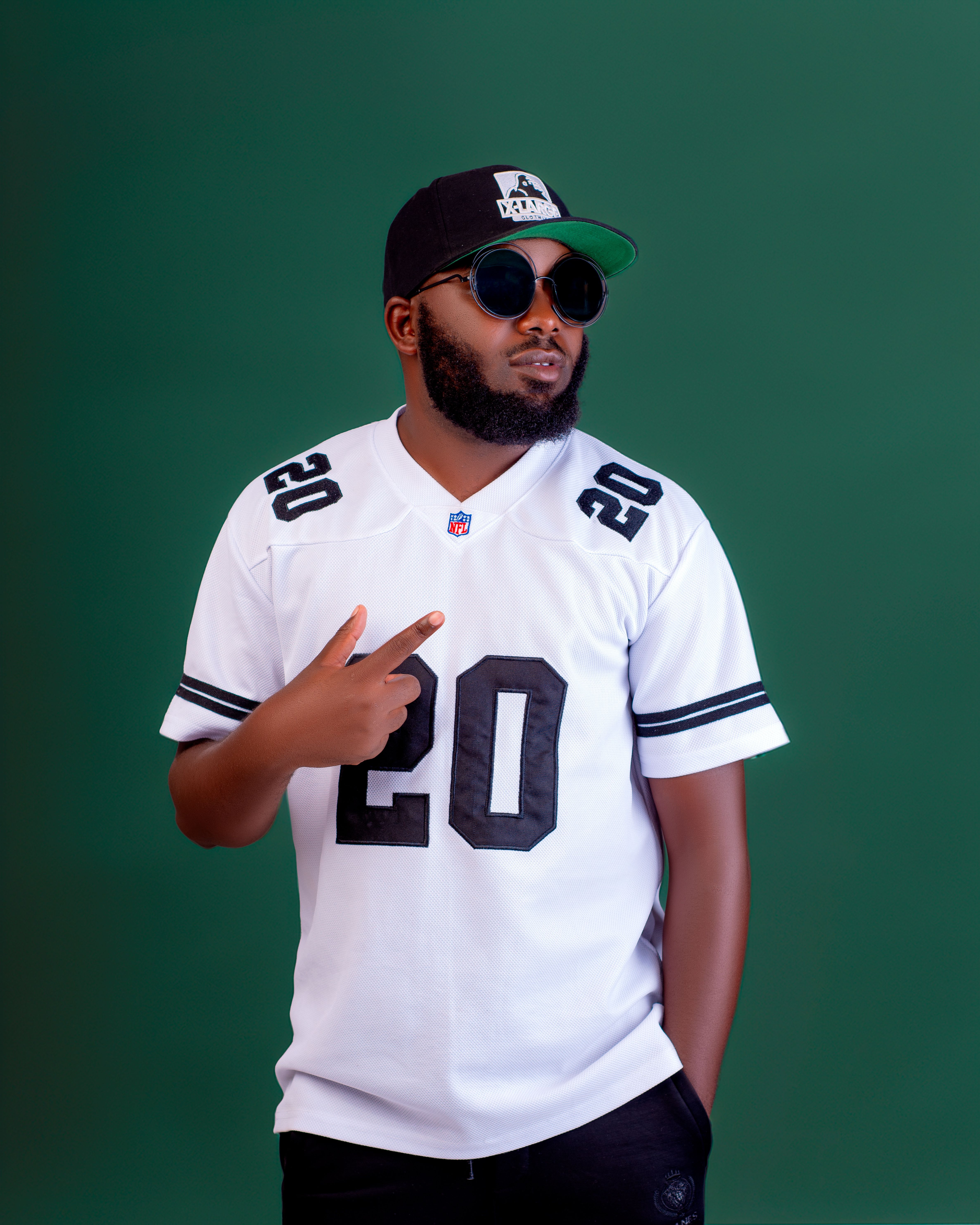 Man wearing sporty white jersey and sunglasses with a cool demeanor on green background.