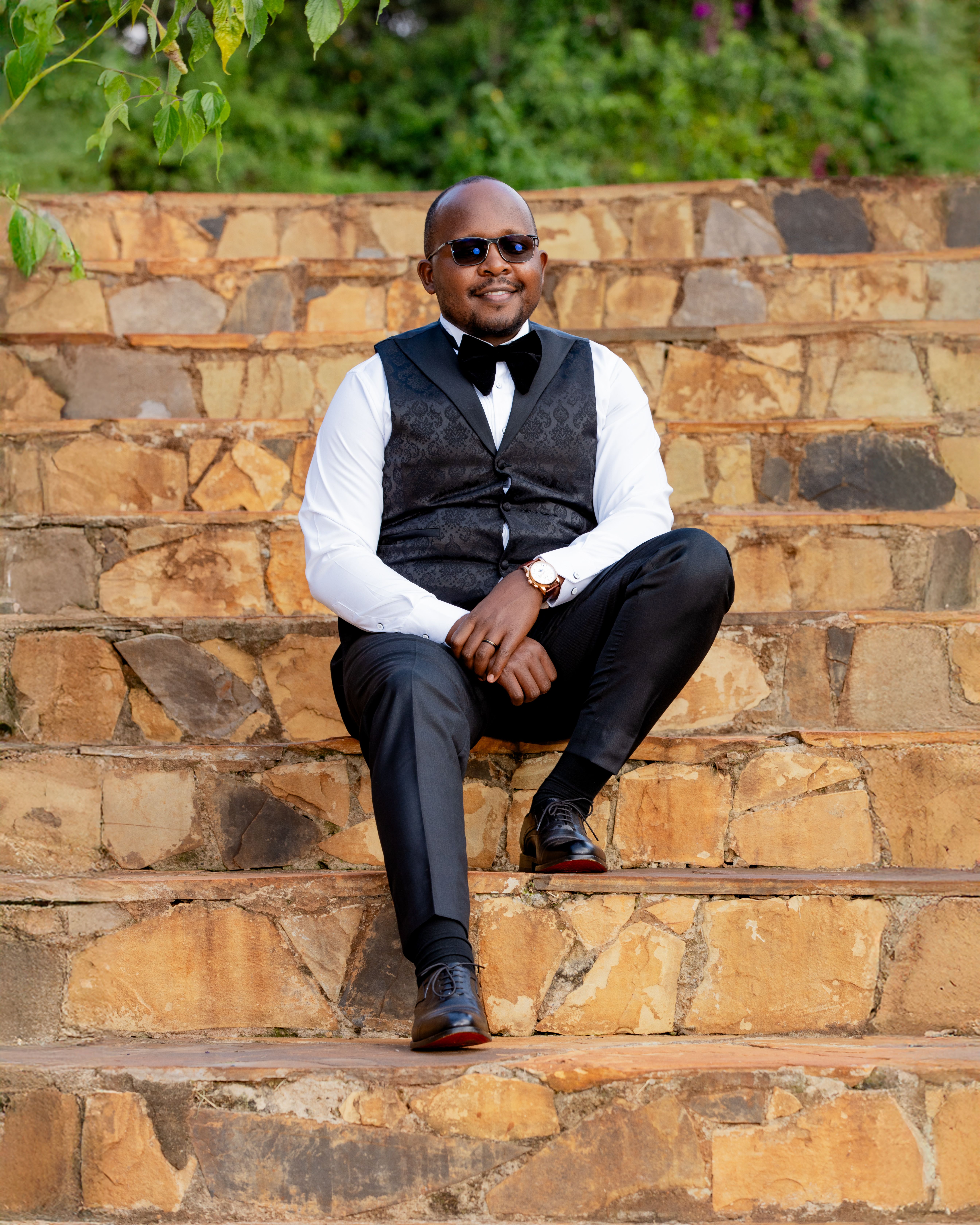Smiling man in sunglasses with formal vest sitting on outdoor stone steps.